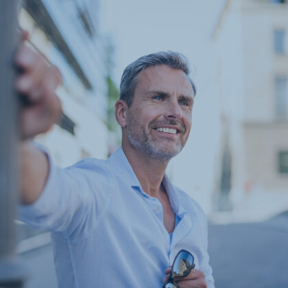 Ein sympathischer Mann mittleren Alters lehnt entspannt an einer Laterne und lächelt.